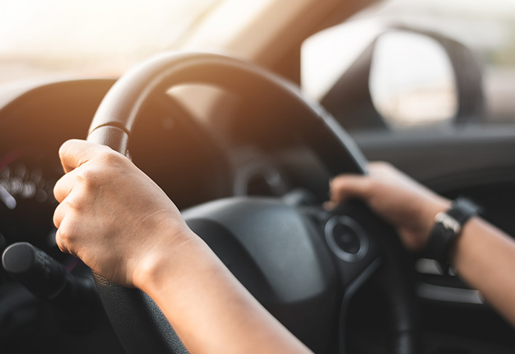 hands gripping a steering wheel driving a car focused on the road 4 key elements of safe driving