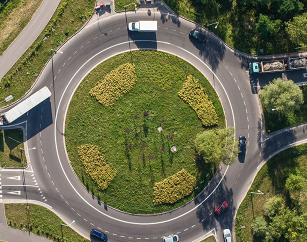 aerial view of a roundabout with green landscaping and vehicles on the road featuring three prominent green patches in the center