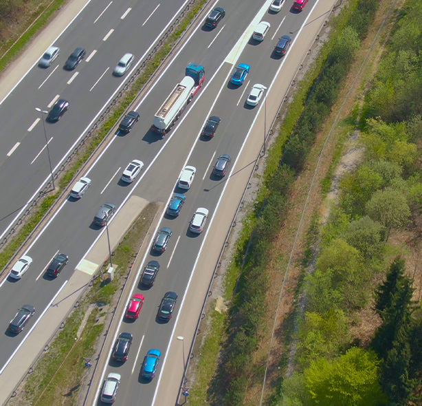 cars driving on a highway surrounded by trees with a bridge in the background showcasing 4 lanes of traffic