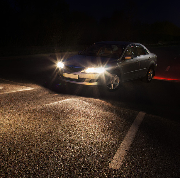 car on a dark road with headlights illuminating the scene and visible parking lines showcasing night driving safety tips and three illuminated areas nearby